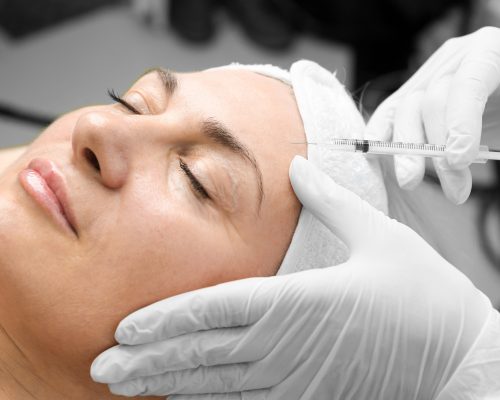 Young caucasian woman getting botox cosmetic injection in a forehead. Beautiful woman gets botox injection in her face. Adult girl gets cosmetic injection of botox in a clinic. Beauty treatments